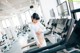 A woman is standing on a treadmill in a gym.