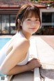 A woman in a white bathing suit leaning on the edge of a swimming pool.