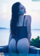 A woman in a black bathing suit sitting on the edge of a pool.