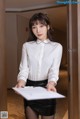 A woman in a white shirt and black skirt holding a clipboard.